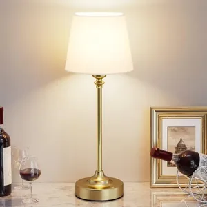 A table lamp with a gold base and a white shade is placed on a marble surface, surrounded by wine bottles, a wine glass, and a framed picture.