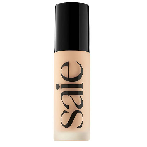 A Saie foundation bottle with a clear body, showing light beige liquid, and a black cap.