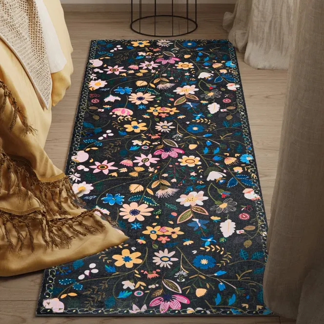 Floral-patterned rug featuring colorful flowers on a dark background, placed beside a bed with a yellow fringed blanket.