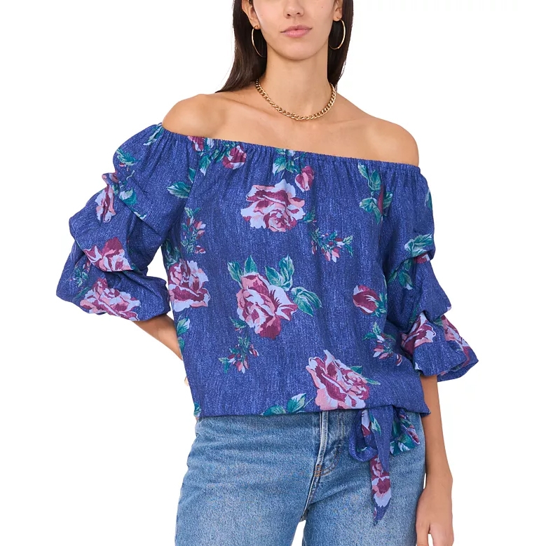 Blue off-the-shoulder top with pink and purple floral print, featuring ruched three-quarter sleeves and waist tie detail, paired with light blue jeans.