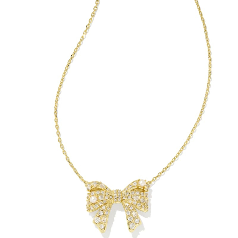 A gold necklace featuring a bow-shaped pendant adorned with sparkling stones and pearls, suspended on a delicate chain.