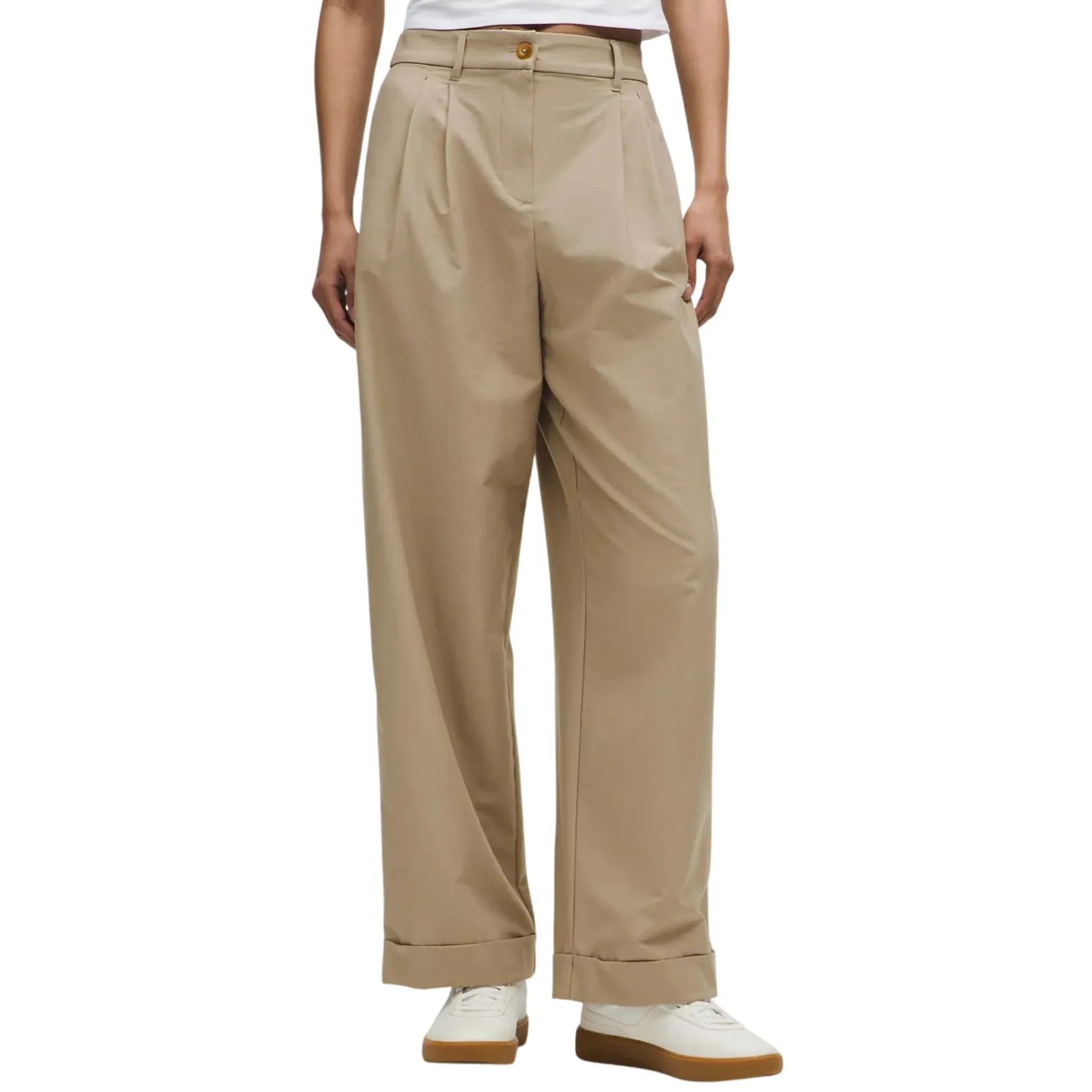A person is wearing high-waisted, pleated, wide-leg khaki pants paired with white sneakers.