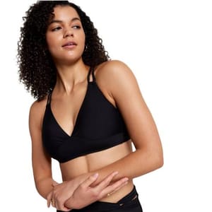 A woman in athletic wear poses, wearing a black sports bra with a strappy design.