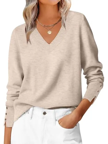 A beige V-neck sweater with buttoned cuffs is paired with white pants. The outfit is accessorized with a necklace featuring a round pendant.