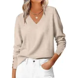 A beige V-neck sweater with buttoned cuffs is paired with white pants. The outfit is accessorized with a necklace featuring a round pendant.