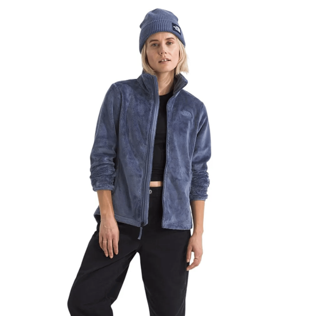 A person wearing a blue fleece jacket, black cropped pants, beanie, white socks, and gray sneakers.