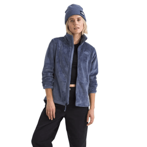 A person wearing a blue fleece jacket, black cropped pants, beanie, white socks, and gray sneakers.