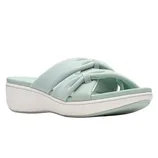 A light green slip-on sandal features a knotted cross-strap design, with a comfortable cushioned sole and a low wedge heel.