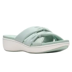 A light green slip-on sandal features a knotted cross-strap design, with a comfortable cushioned sole and a low wedge heel.