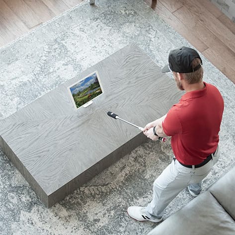 A man is using a selfie stick to take a photo of a laptop screen on a modern table.