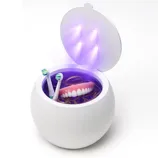 A UV sterilizer for dental items, containing a pair of dentures, electric toothbrush heads, and a golden ring, is opened with four UV lights visible inside.