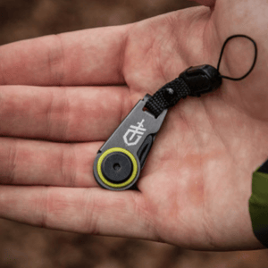 A compact, handheld Gerber tool with a lanyard, featuring a logo and a circular component with a yellow accent, suggestive of a utility or outdoor gadget.