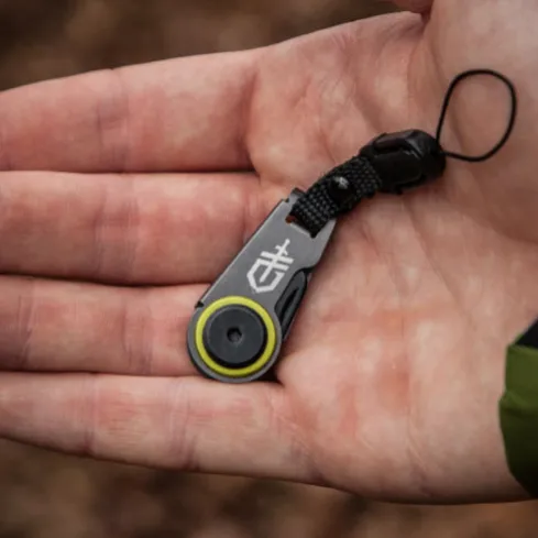 A compact, handheld Gerber tool with a lanyard, featuring a logo and a circular component with a yellow accent, suggestive of a utility or outdoor gadget.