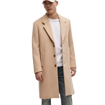 A beige single-breasted topcoat with notch lapels and three buttons, worn over a white shirt and jeans. The coat features pockets and a classic, tailored fit, paired with a casual white cap.