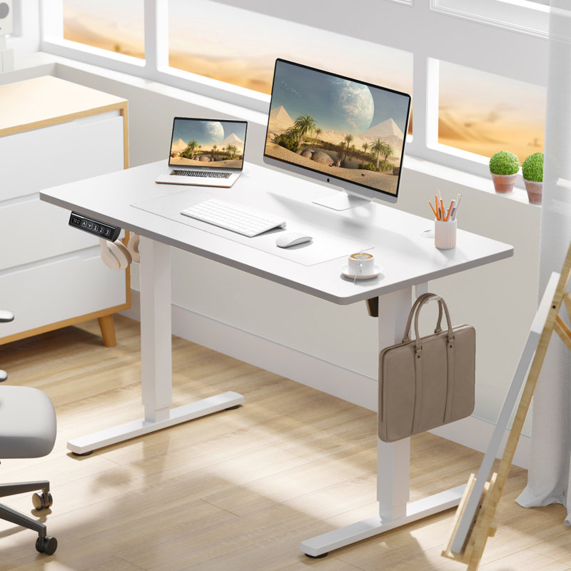 A modern white adjustable standing desk with a laptop, monitor, keyboard, mouse, and cup. Accessories include headphones, a pencil holder, and a briefcase hanging from the desk. The desk stands on a hardwood floor, with a cozy and minimalistic setup.