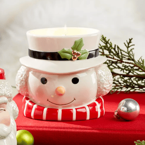 A candle holder shaped like a snowman's head with a lit candle on top, accompanied by holiday decorations.