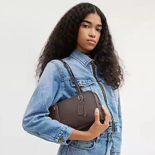 A person is wearing a light blue denim jacket and holding a small brown crossbody bag.