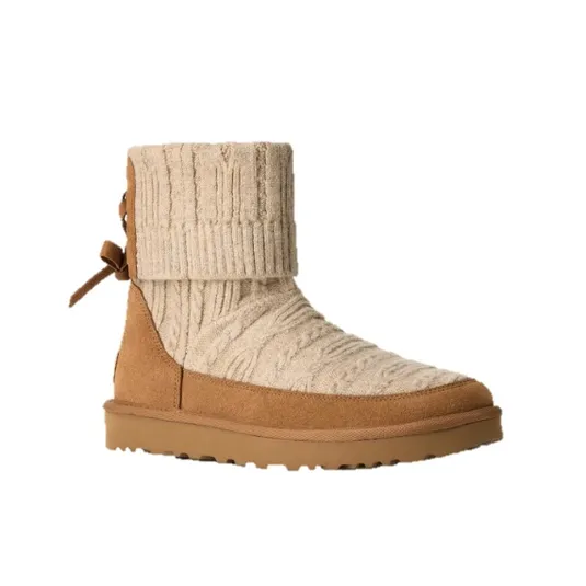 A tan suede and knit ankle boot featuring a fold-over cuff with a cable-knit design and a bow detail on the back. The sole is flat with a textured pattern for traction.