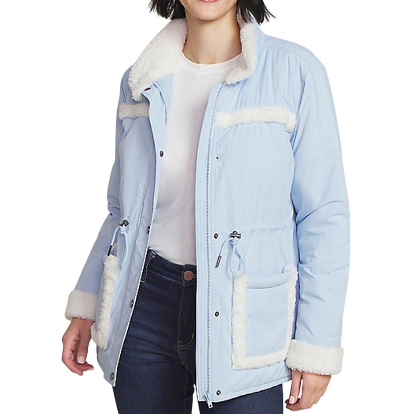Light blue jacket with white sherpa trim on the collar, cuffs, and pockets, featuring a drawstring waist and snap-button details, worn over a white shirt and paired with dark jeans.