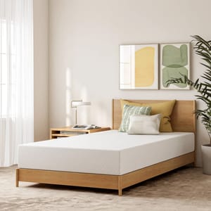 An 8\“ gel memory foam mattress lies on a wooden bed frame, accompanied by neutral-toned pillows, a small bedside table with a lamp, and decorative wall art.
