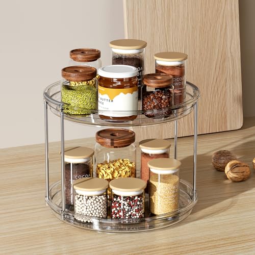 Two-tier clear rotating spice rack organizer holding glass jars with wooden and gold lids, storing various spices and dry goods on a wooden surface.