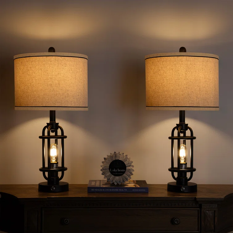 Two table lamps with cylindrical shades and industrial-style bases, turned on and illuminating a wall.