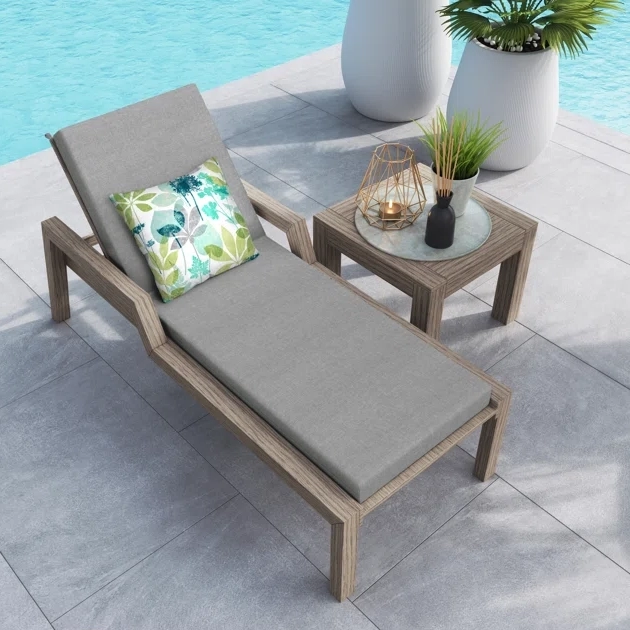 Outdoor lounge chair with gray cushion and decorative pillow, accompanied by two wood-finish side tables adorned with a candle lantern and vase.