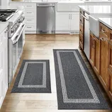 A kitchen with hardwood floors features two dark gray rugs with a light-colored border. The space includes stainless steel appliances, white cabinets, and wooden accents.