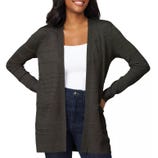 A woman wears a dark gray open-front cardigan over a white top and dark jeans, with her hands in her pockets.