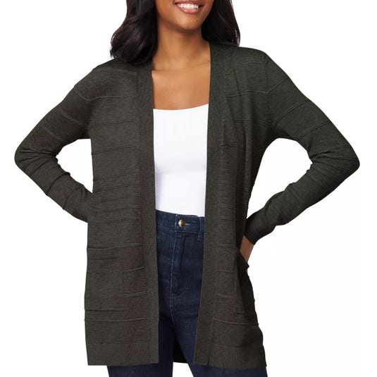 A woman wears a dark gray open-front cardigan over a white top and dark jeans, with her hands in her pockets.