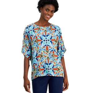 A woman wearing a colorful, geometric-patterned top with a floral design in blue, orange, and green hues, paired with navy blue pants.