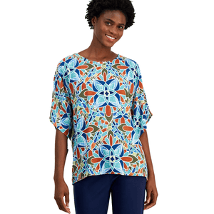 A woman wearing a colorful, geometric-patterned top with a floral design in blue, orange, and green hues, paired with navy blue pants.