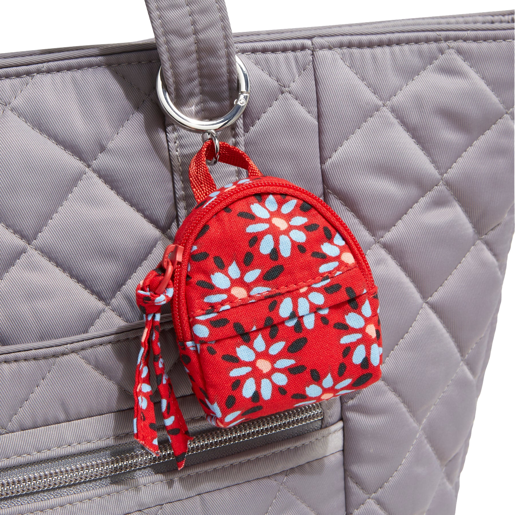 A quilted gray tote bag features a small, red floral-patterned keychain in the shape of a backpack attached to its handle.