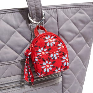 A quilted gray tote bag features a small, red floral-patterned keychain in the shape of a backpack attached to its handle.