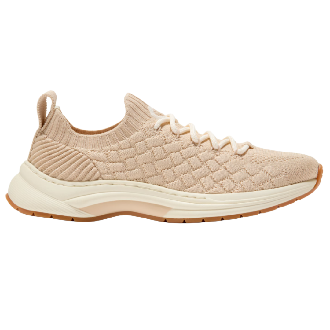 A beige knit sneaker with a quilted pattern, lace-up front, and pull tab on the heel. The shoe features a cushioned sole with a textured rubber bottom.