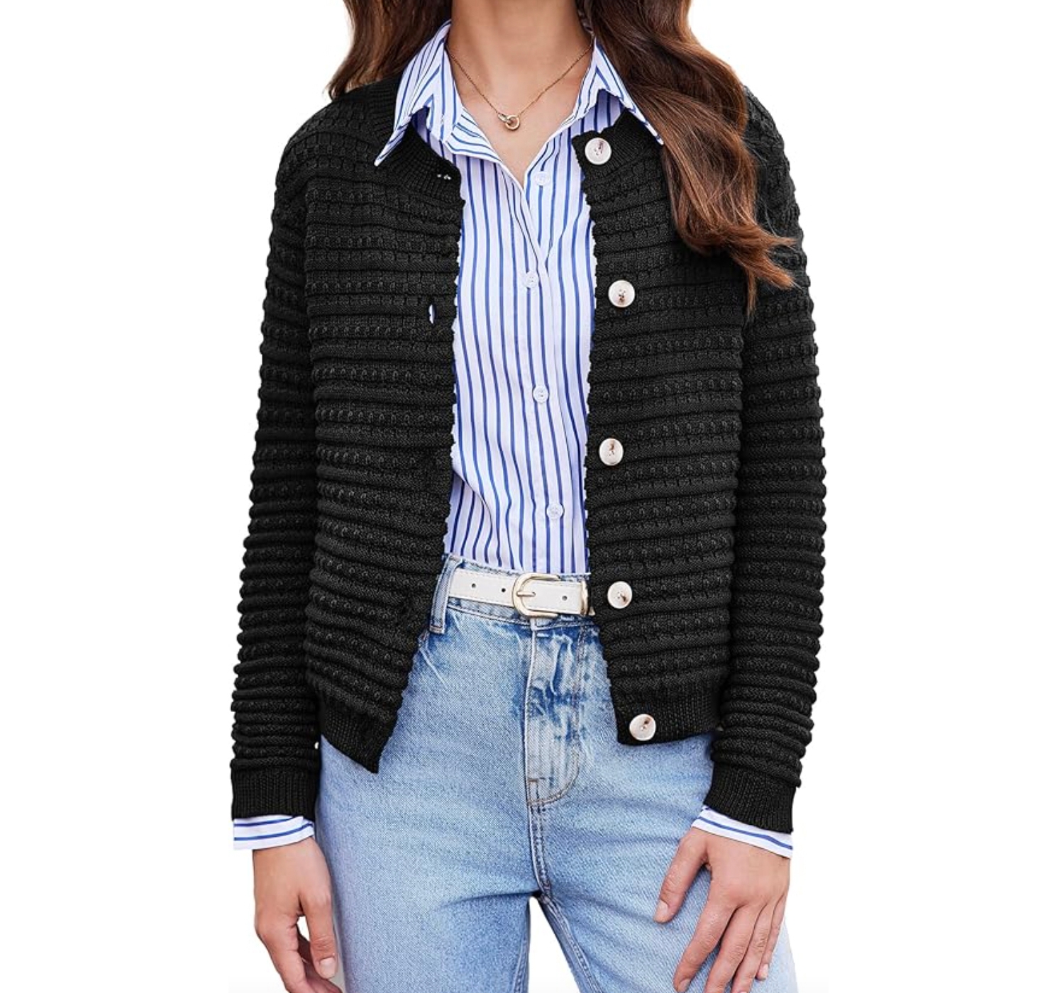 A woman is wearing a black knit cardigan over a blue and white striped button-up shirt, paired with light blue jeans and a white belt.