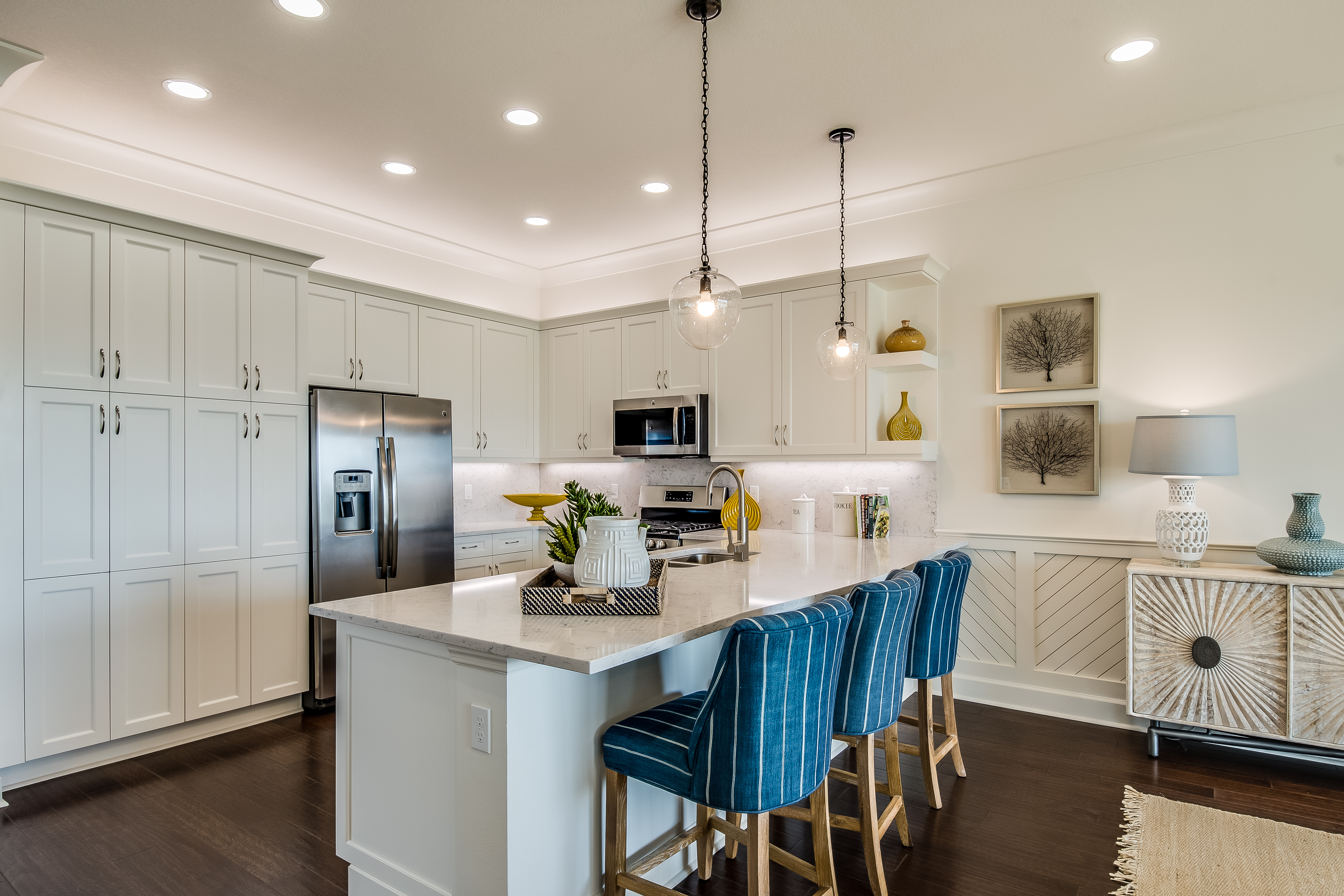Modern kitchen with stainless steel appliances, white cabinetry, and blue upholstered bar stools at the island.