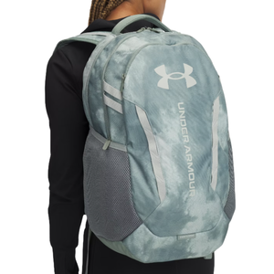 A light blue Under Armour backpack with a marbled pattern, featuring the Under Armour logo, side mesh pockets, and adjustable straps.