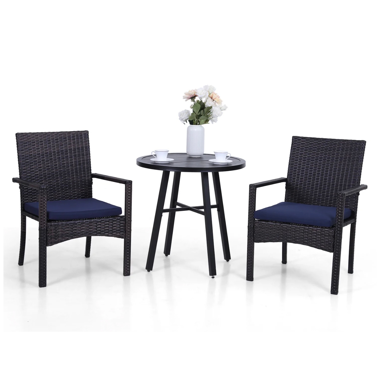 A 3-piece patio bistro set featuring two rattan-style armchairs with navy cushions and a round, black metal table. The table has a vase with flowers and two cups on it.