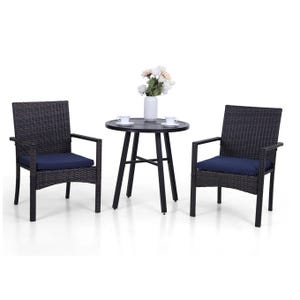 A 3-piece patio bistro set featuring two rattan-style armchairs with navy cushions and a round, black metal table. The table has a vase with flowers and two cups on it.