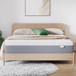 A modern wooden bed frame with a gray and white mattress is topped with beige bedding and green accent pillow. A textured gray rug lies on the floor, and abstract art decorates the wall above.