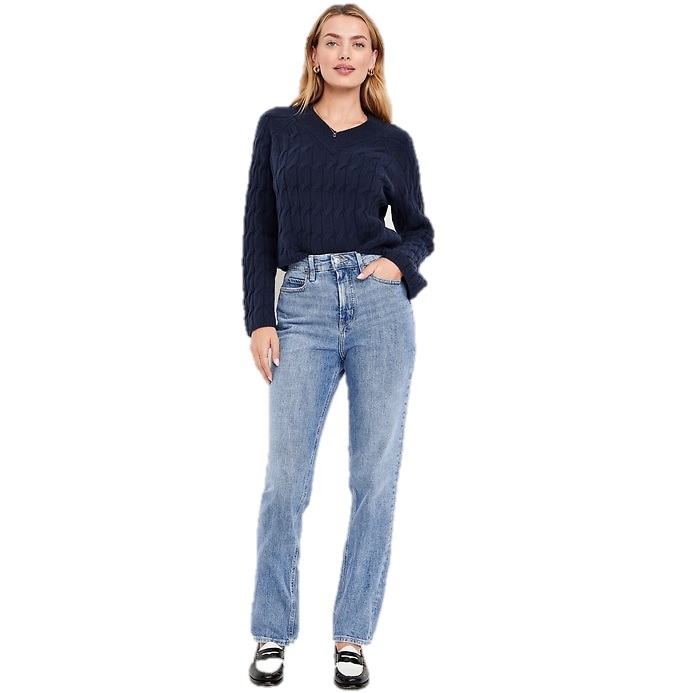 A woman is wearing a navy cable-knit sweater and light blue straight-leg jeans, paired with black loafers.