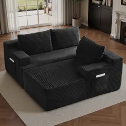A black, corduroy-textured sofa with a chaise lounge features side pockets for storage, set on a beige rug in a living room with wooden floors and a fireplace.