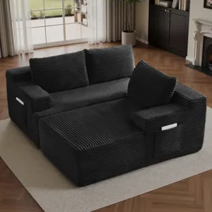 A black, corduroy-textured sofa with a chaise lounge features side pockets for storage, set on a beige rug in a living room with wooden floors and a fireplace.