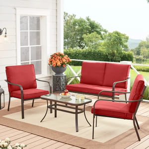 Outdoor patio furniture set with a red loveseat, two chairs, a glass-top table, and a decorative vase on a beige rug.