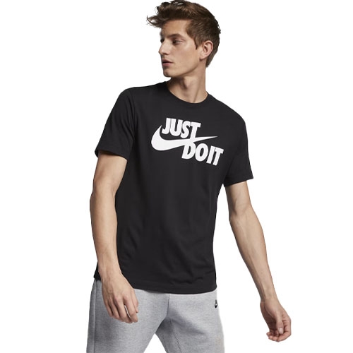 Black Nike T-shirt with \“JUST DO IT\“ in bold white letters across the chest, featuring the iconic swoosh logo. Worn with gray sweatpants.