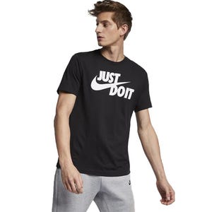 Black Nike T-shirt with \“JUST DO IT\“ in bold white letters across the chest, featuring the iconic swoosh logo. Worn with gray sweatpants.