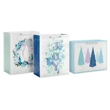 Three festive blue-themed gift bags feature designs with a wreath, the word \“JOY\“ with florals, and abstract Christmas trees, each with ribbon handles.
