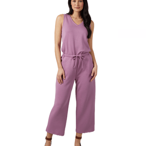 A woman is wearing a sleeveless, lavender-colored jumpsuit with a V-neck and wide-leg pants, tied at the waist with a drawstring.