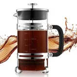 A French press coffee maker with a transparent glass body, stainless steel frame, and black handle, showing measurement markings. It's filled with coffee against a splash background.